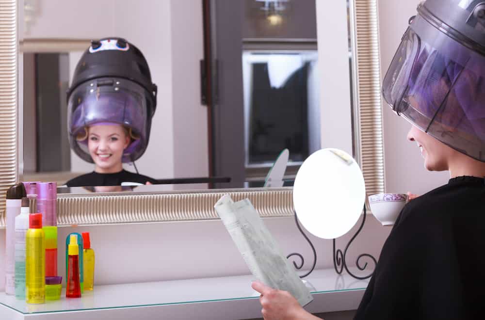 Girl reading magazine drinking coffee. Hairdryer in hair beauty salon